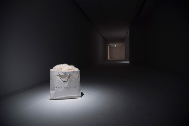 「ホワイト・ギフト」（2016）。暗く細長い空間から始まる最初の作品。ロンドンの人気百貨店の紙袋に入れられた毛皮のコートが、ホワイトデーのプレゼントを思わせる。